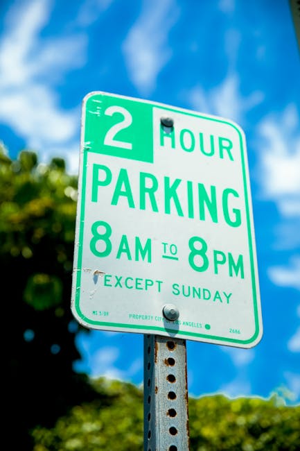 A blue parking sign mounted on a pole beneath a greenish roof in an outdoor setting, indicating that parking is reserved for vans that are accessible for disabled individuals. The sign clearly states it is for 'PARKING ONLY VAN ACCESSIBLE' with a wheelchair symbol above the text. Additional information on the sign mentions a minimum fine of $250 for violations. The background shows a roof and part of a building structure, suggesting an urban or residential area where vehicle loading zones are designated for home relocation and furniture transport. This parking restriction is relevant for relocation services, such as those offered by Man With a Van Clapton, emphasizing the importance of parking rules when conducting house removals or furniture transport in the Clapton area.